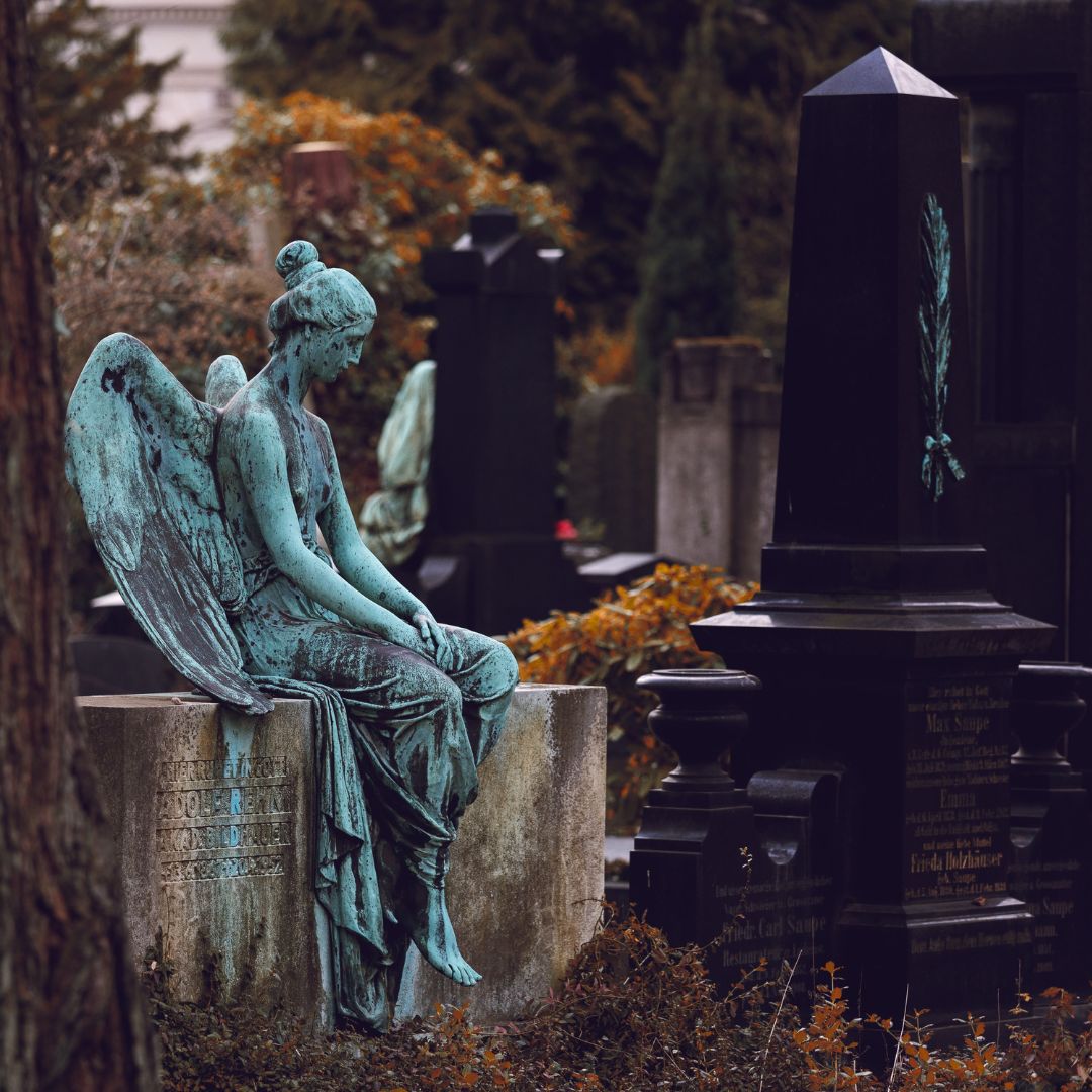 cmentarz na nagrobku siedzi smutny anioł kobieca postać ze skrzydłami w tle inne nagrobki