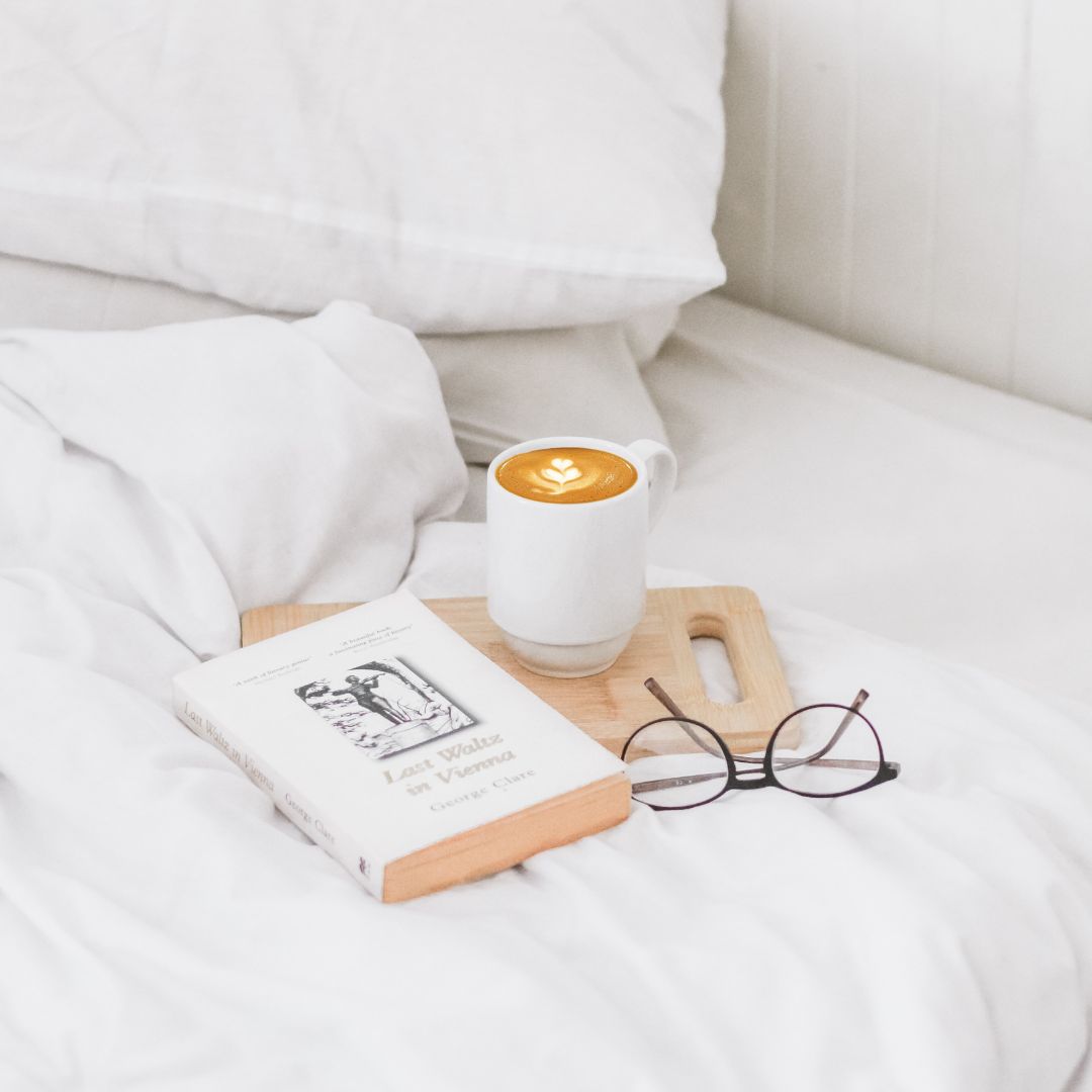 pościel na łóżku kawa książka i okulary do czytania